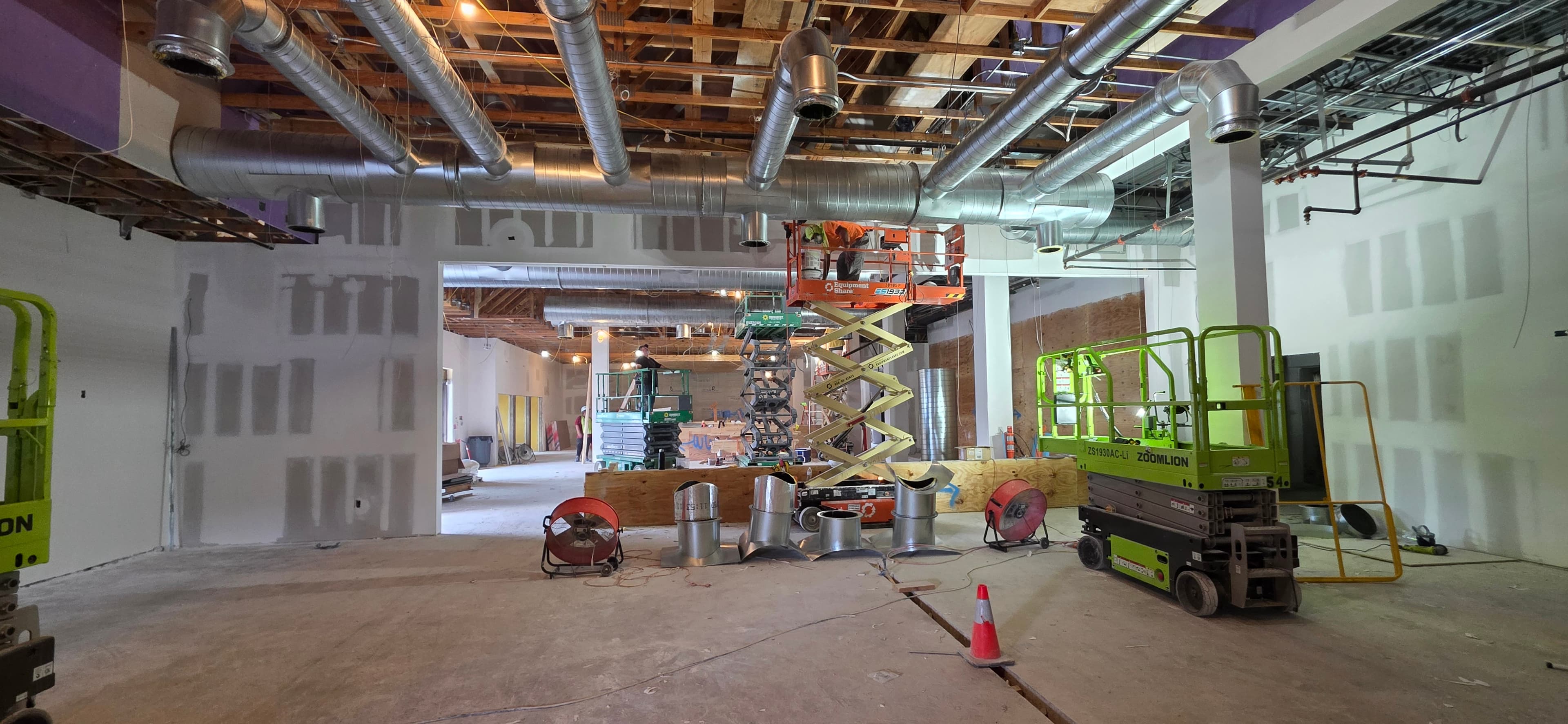 Workers using scissor lifts to install metal ductwork in an unfinished commercial building interior.