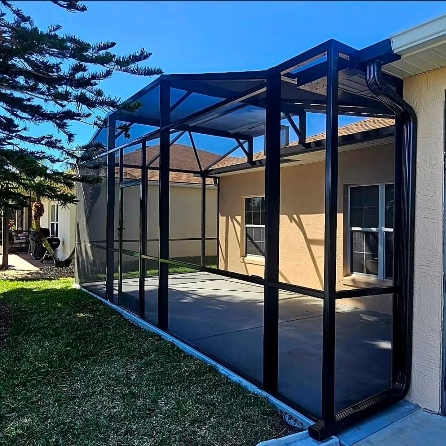 Black aluminum screen enclosure with a gabled roof attached to a tan stucco house.