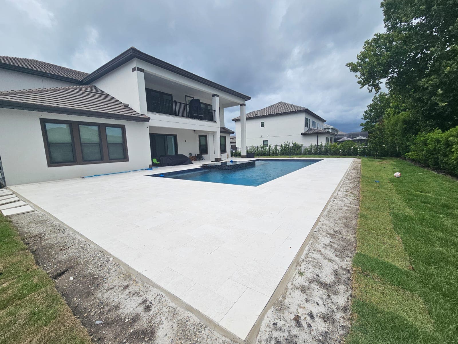 Modern two-story white house featuring a large stone patio and a rectangular swimming pool.