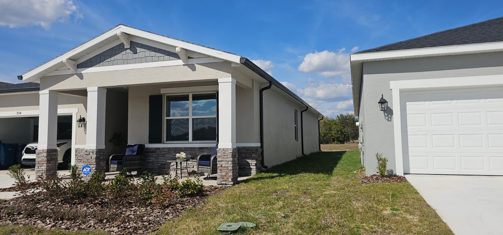 Modern gray house with white trim and a stone-pillared front porch under a blue sky.
