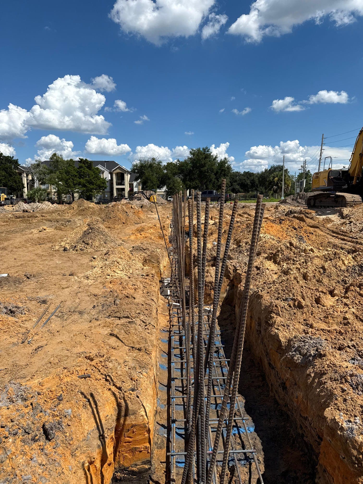 Steel rebar foundation cage inside a deep trench at a sunny outdoor construction site.