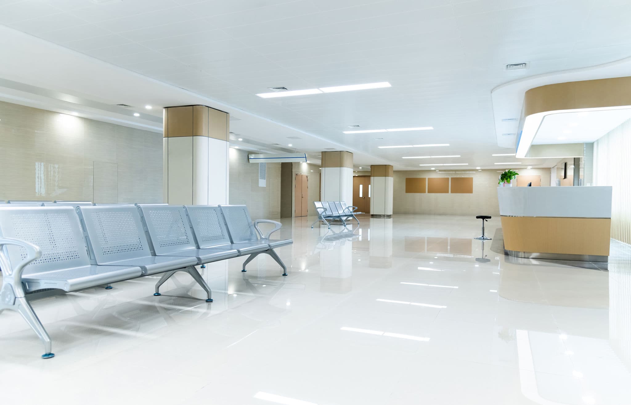 Bright, empty hospital waiting area with rows of silver metal chairs and a reception desk.